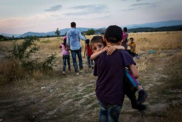 © ACNUR/A. McConnell.  Un joven refugiado sirio lleva en brazos a su hermano a través de la frontera entre Grecia y la Antigua República Yugoslava de Macedonia, cerca Eidomeni, Grecia.